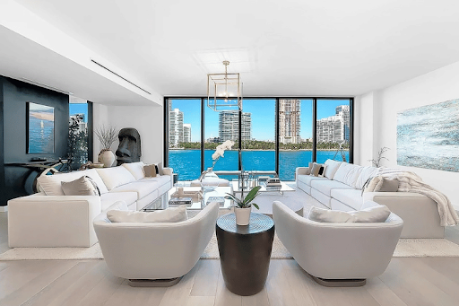 Modern living room with different types of couches, including two modular sofas and chairs facing waterfront view through large windows.